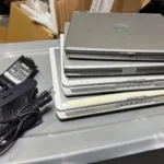 Chồng laptop cũ và bộ sạc thể hiện sự lãng phí tài nguyên công nghệ